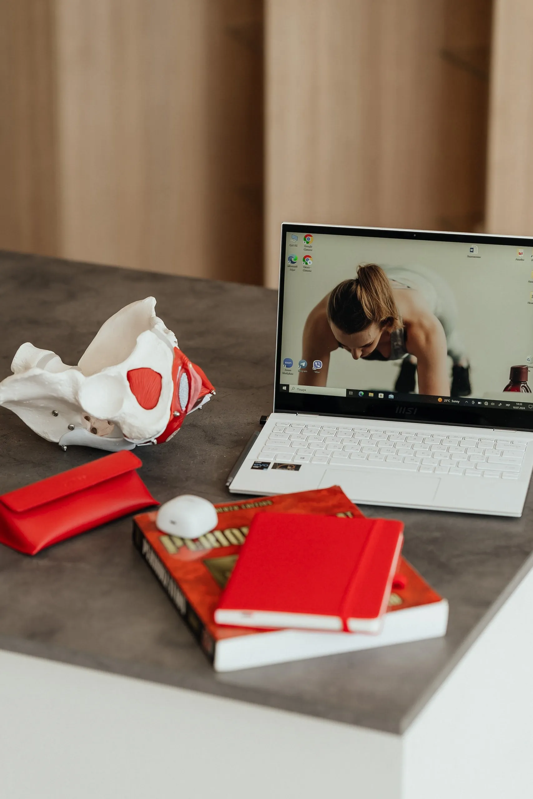 Ноутбук із тренуванням, модель тазу з червоними м'язами та щоденники на столі